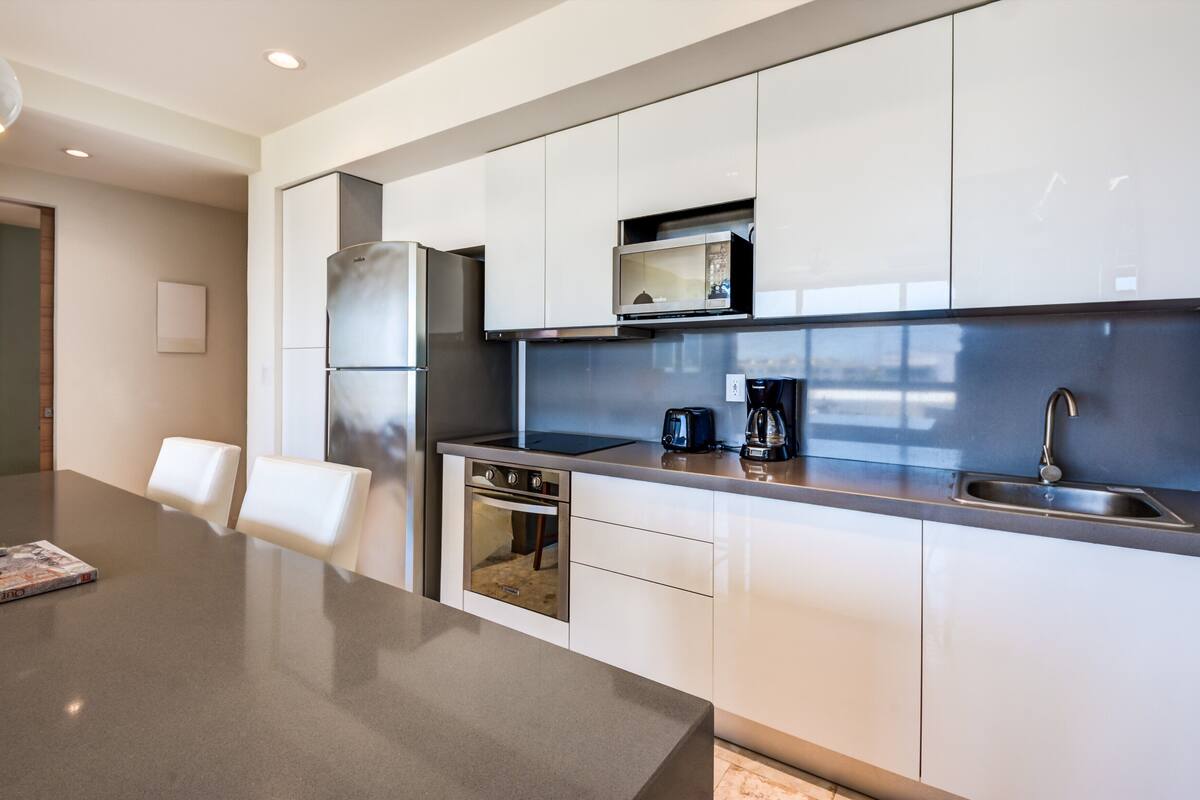 A modern kitchen with white cabinets, stainless steel appliances, a built-in microwave, and a coffee maker.