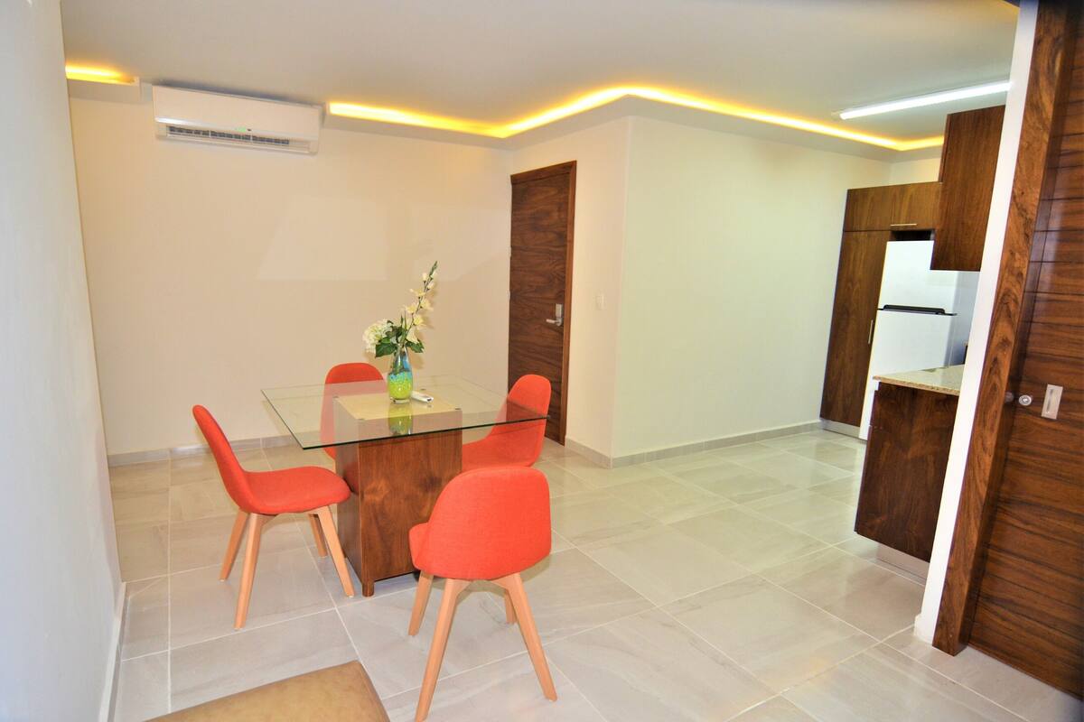 A modern kitchen with a glass dining table, red chairs, and wooden cabinets.