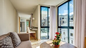 A modern living room with a sofa, a dining table with a vase of flowers, and large windows offering a view of the city. - Carmen Sol Rentals Apartamentos (Playa del Carmen)
