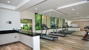 A gym with treadmills, a reception desk, and large windows with a view of greenery. - Carmen Sol Rentals Apartamentos (Playa del Carmen)