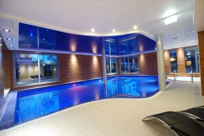 An indoor swimming pool with a curved design, glass walls, and a tiled floor. - Puchacz Spa (Rewal)