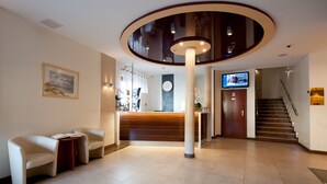 Eine Hotellobby mit einer Rezeption, zwei Sofas, einer Uhr, einem Fernseher und einer Treppe.