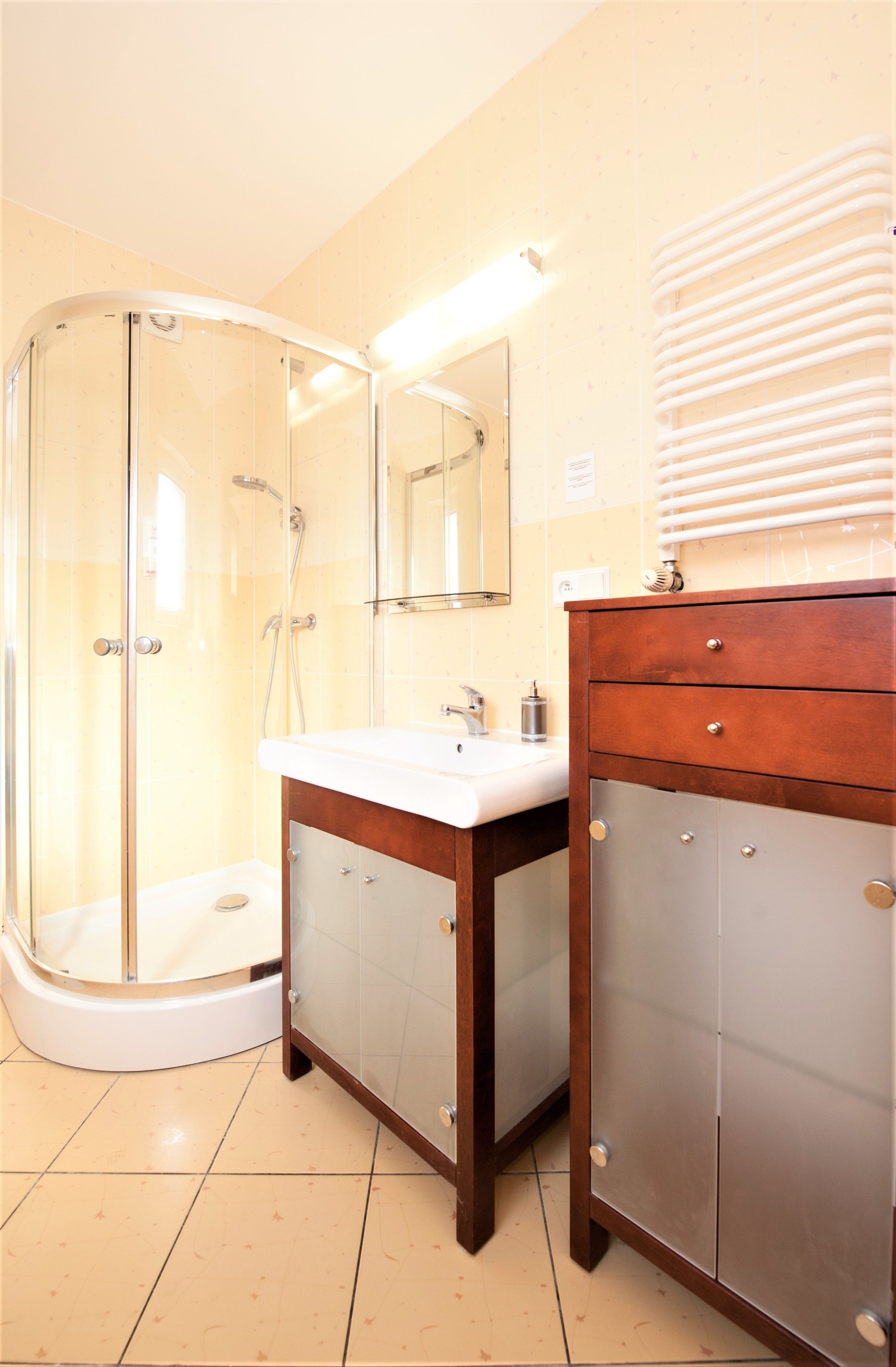 A bathroom with a glass shower enclosure, a white sink, and a wooden vanity with drawers.