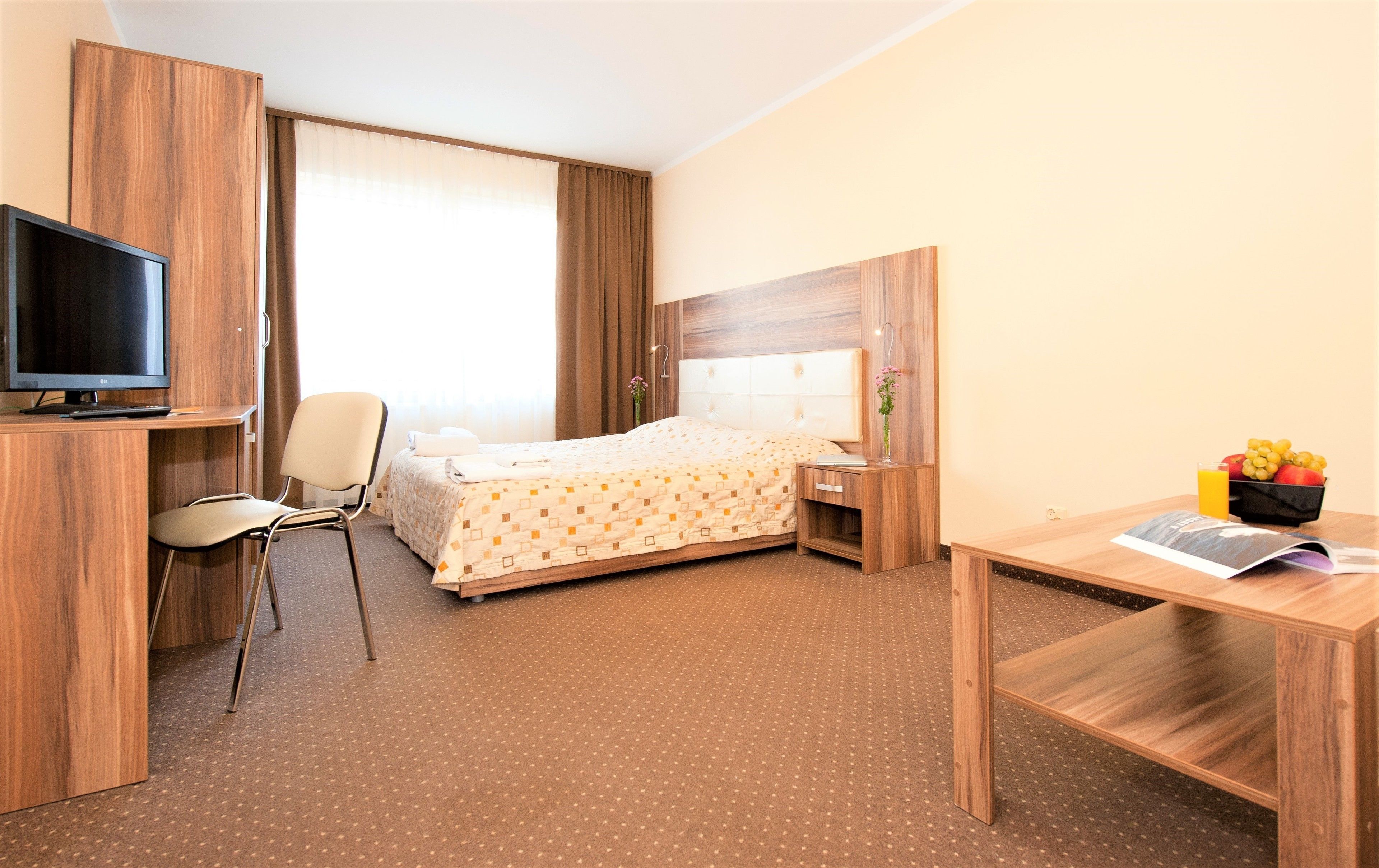 A hotel room with a bed, desk, chair, TV, and a small table with fruit.