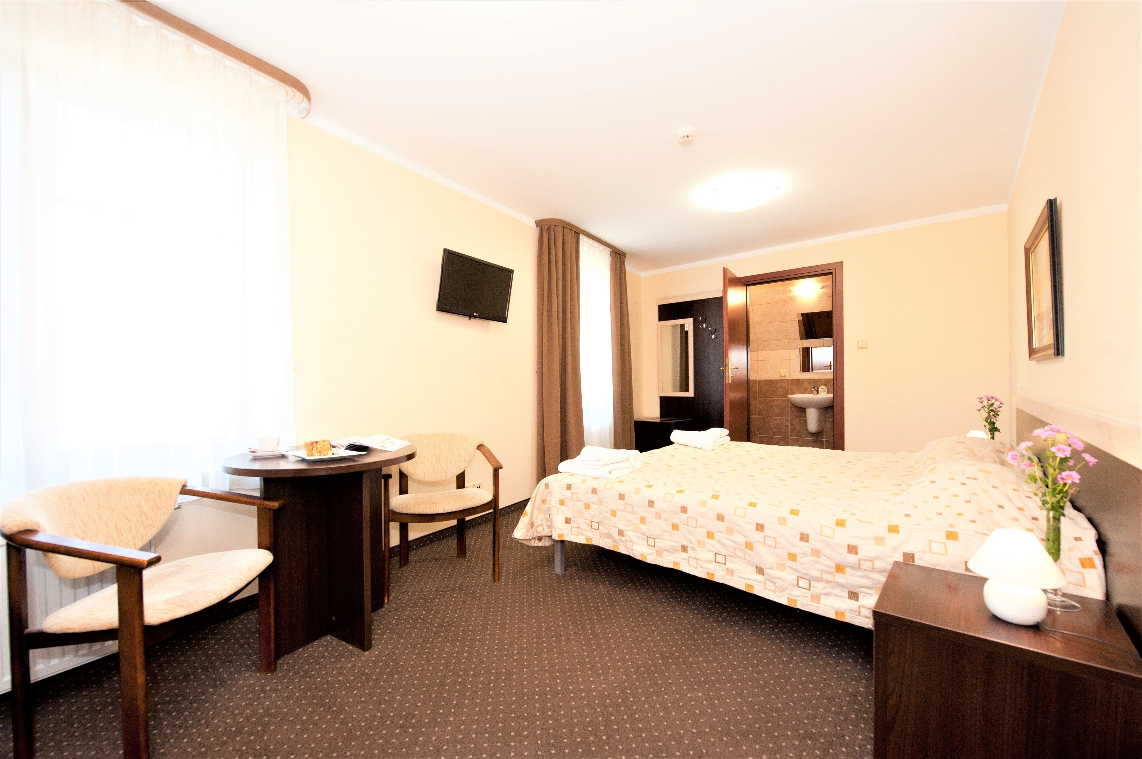 Habitación de hotel con cama, escritorio, silla, televisión y baño visible a través de una puerta abierta.