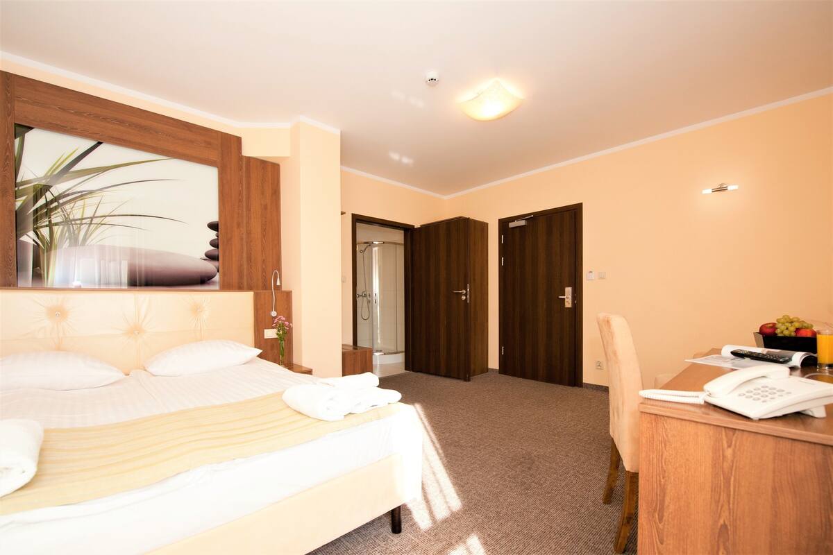 A hotel room with a bed, a desk with a phone, a mirror, and a door leading to a bathroom.