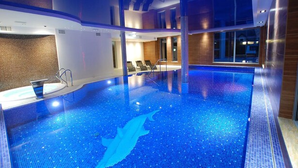 Ein Innenpool mit Delfin-Motiv auf dem Boden, Liegestühlen und Blick durch große Fenster nach draußen.