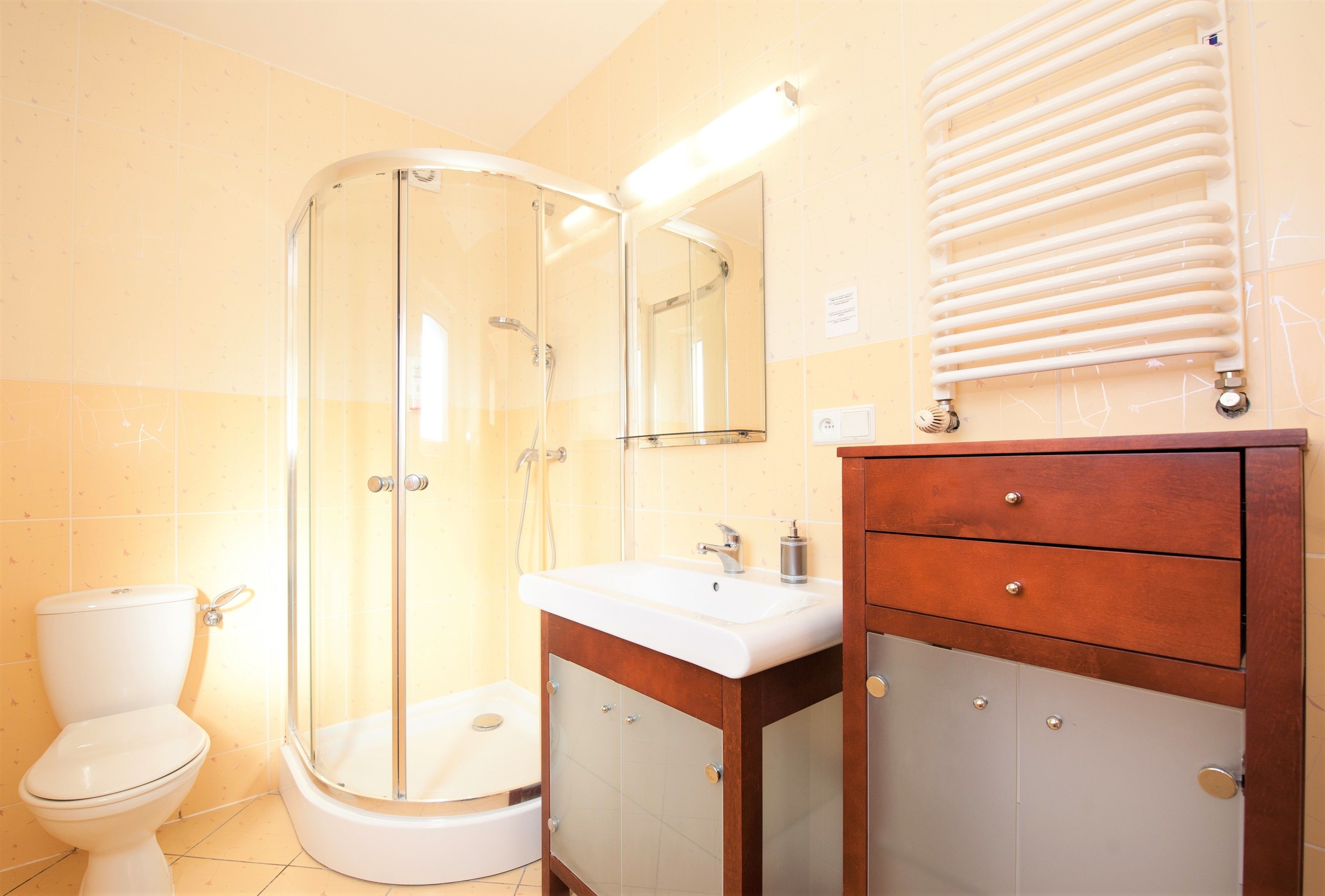 Een badkamer met een douchecabine van glas, een witte wastafel en een houten wastafelmeubel met lades.