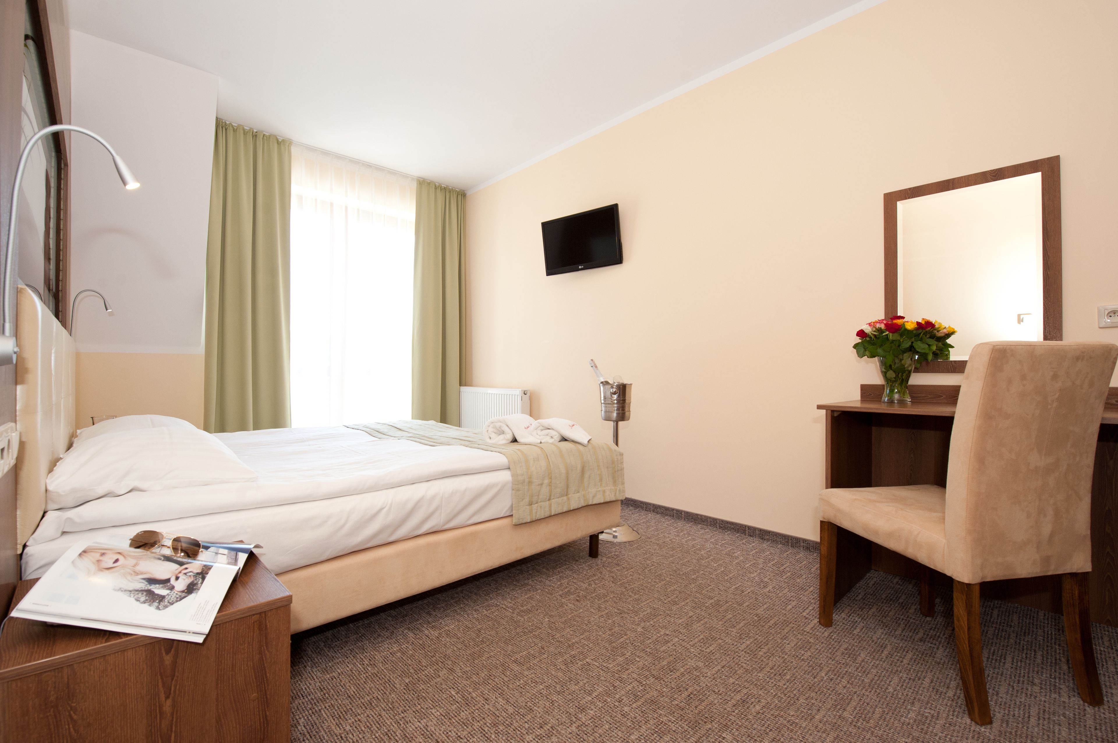 Habitación de hotel con cama, escritorio, silla, televisión y ventana con cortinas.