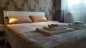 A neatly made bed with folded towels and toiletries, a white headboard, and floral wallpaper. - Verona4rent Giulia (Verona)