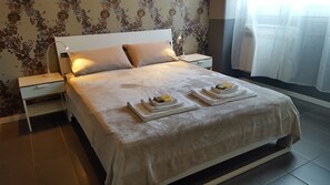 Un letto rifatto con cura, con copripiumino bianco, due cuscini e un comodino con una lampada.