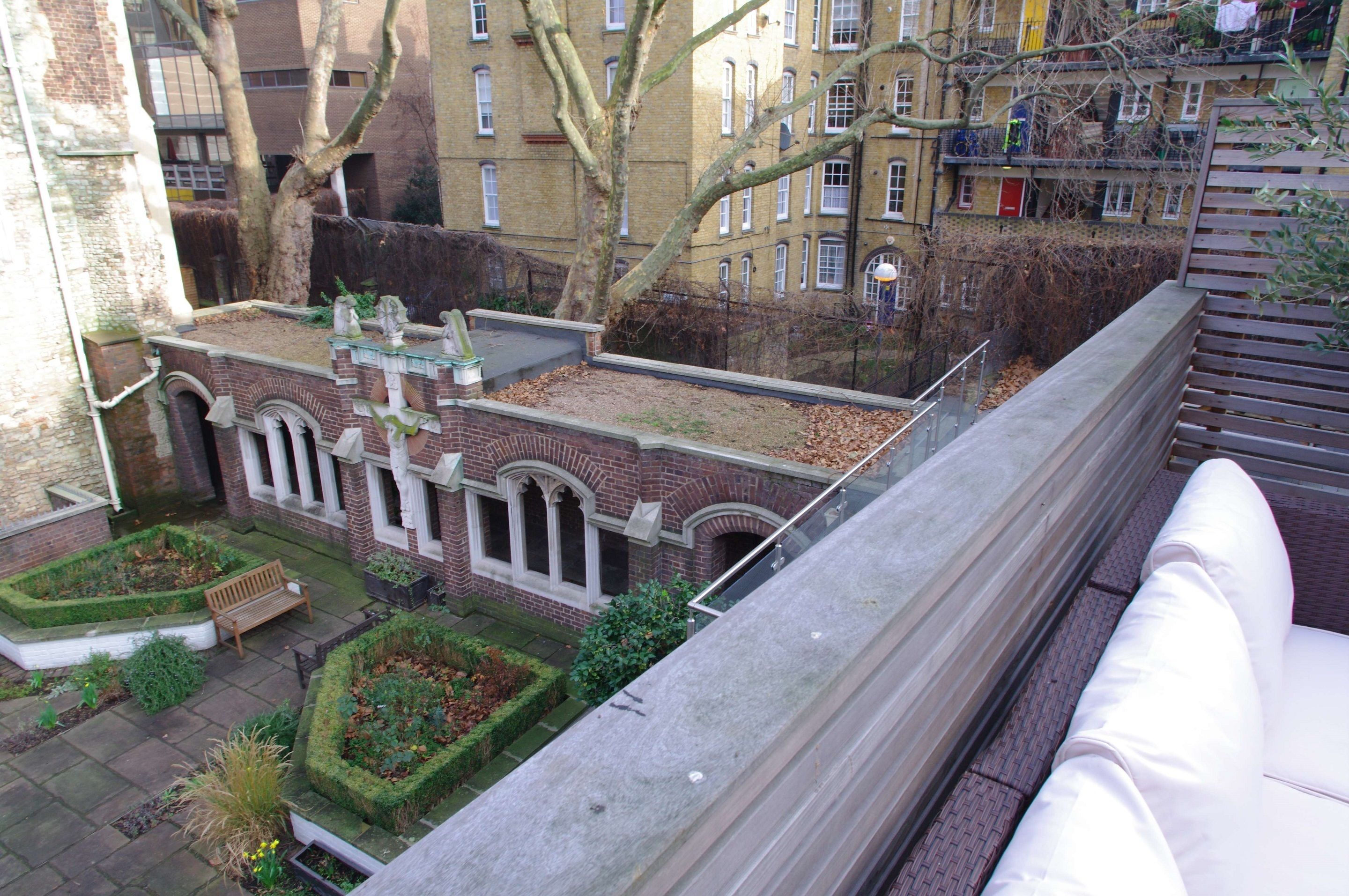 A courtyard with a bench, a small garden, and a building with arched windows.