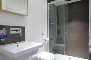 A modern bathroom with a glass-enclosed shower, a white sink, and a toilet.