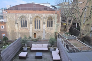 A rooftop terrace with a wooden deck, a sofa set, and potted plants.