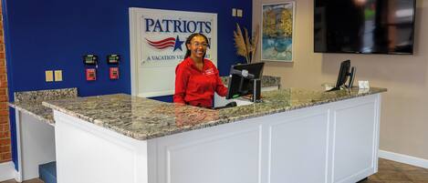 Uma mesa de recepção com uma parede azul, uma placa com a inscrição "Patriots" e uma TV de tela plana fixada na parede.