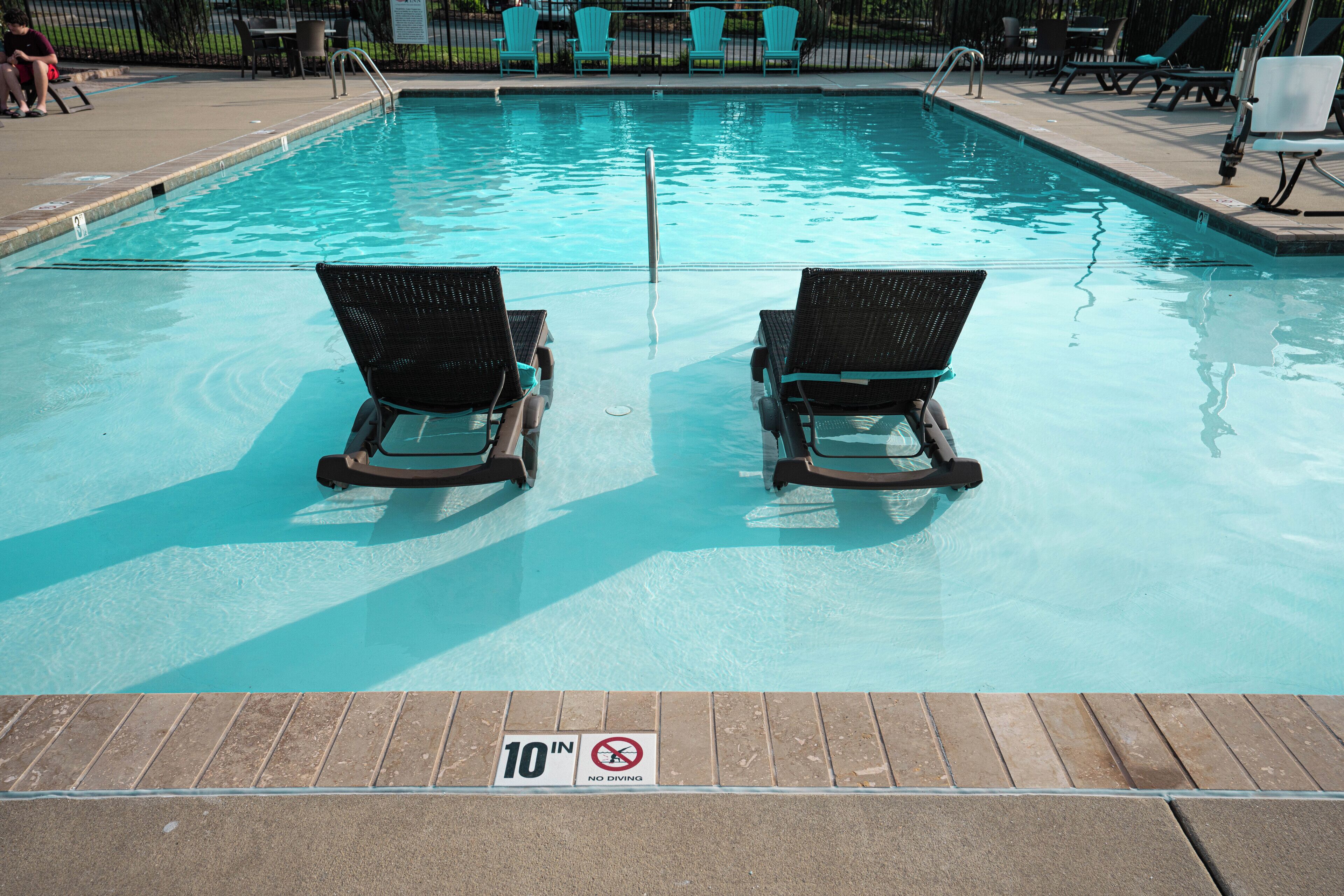 A swimming pool with two lounge chairs facing the water, a 10-inch no diving sign, and a tiled deck area with chairs and tables.