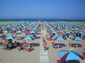 En strand med rader av solstolar och parasoller, en klar himmel och havet i bakgrunden.