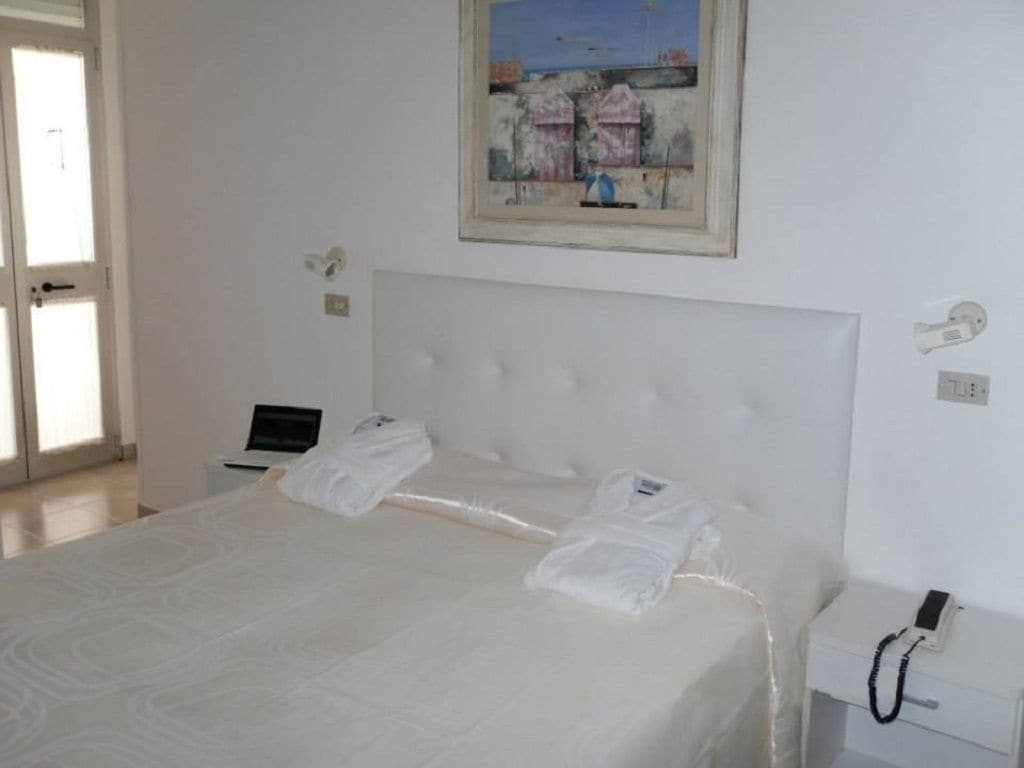 Habitación de hotel con una cama grande, un cuadro en la pared, un escritorio con una computadora portátil y un teléfono.
