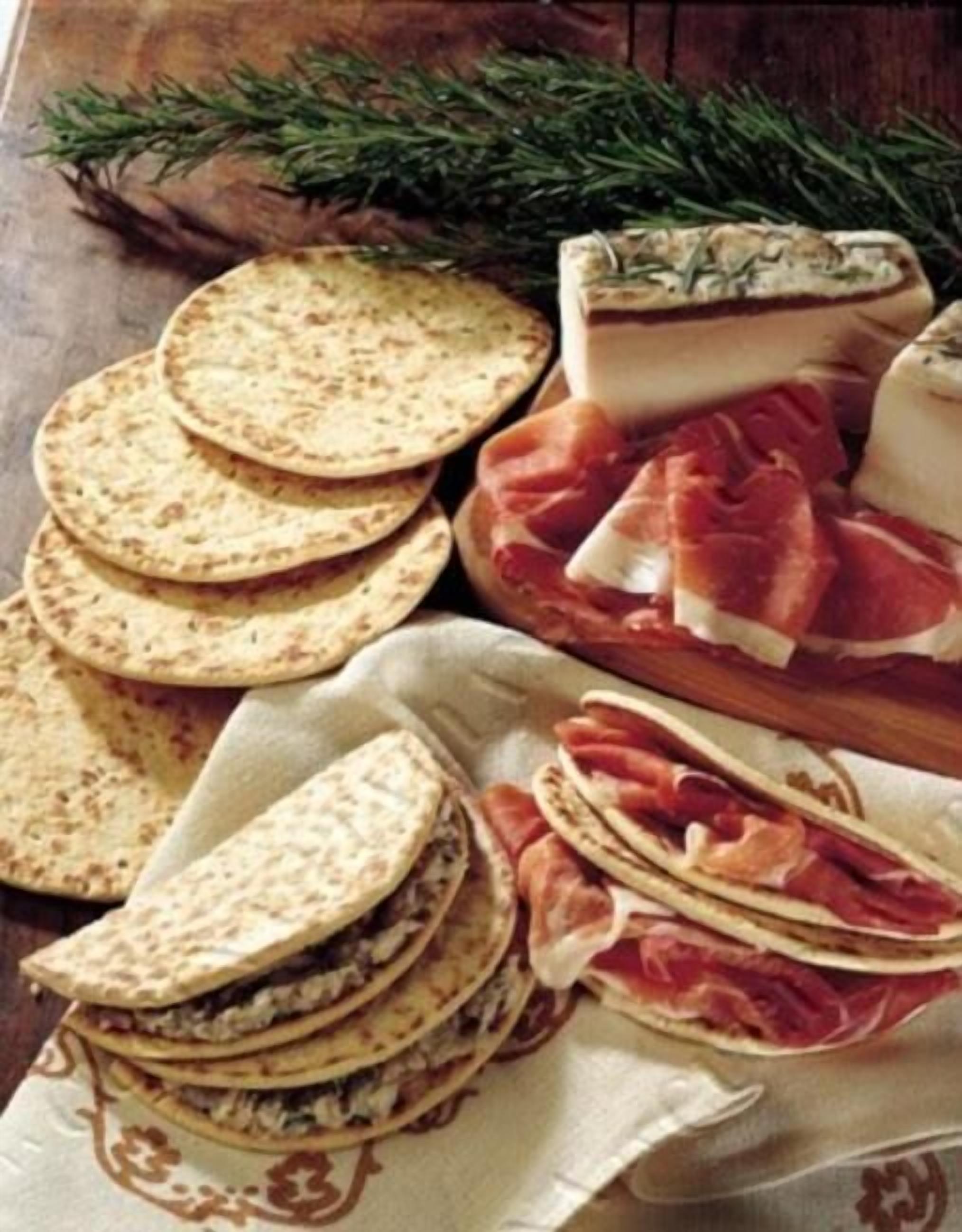 A variety of flatbreads, a block of cheese, and slices of cured meat on a wooden table.