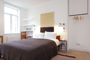 A bedroom with a large bed, a headboard, bedside lamps, a small table, and a window.