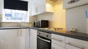A modern kitchen with white cabinets, a black microwave, and a built-in oven. - The London Agent Fitzrovia Studio 1 (London)