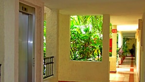 A corridor with a tiled floor, a door on the left, a window with greenery, and a red sign on the wall. - Apartment with pool view RinconadaDelSol (Playa del Carmen)