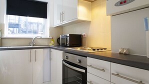 A modern kitchen with white cabinets, a black microwave, and a stainless steel sink. - The London Agent Fitzrovia Studio 2 (London)