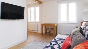 A modern room with a flat-screen TV mounted on the wall, a wooden table with two stools, a bed with patterned bedding, and large windows providing natural light. - The London Agent Fitzrovia Studio 3 (London)