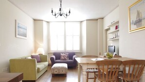 Ein Wohnzimmer mit einem grünen Sofa, einem violetten Sofa, einem Holzespeisetisch mit Stühlen, einer Kronleuchter und einem großen Fenster.