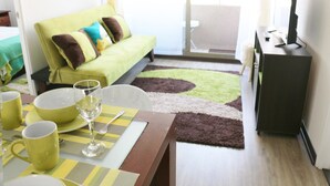 A modern living room with a green sofa, a dining table with yellow placemats, and a flat-screen TV on a stand. - Chile4Rent Eleuterio Ramirez (Santiago)