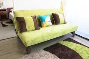 A green sofa with three pillows, a wooden nightstand, and a small table with a lamp.