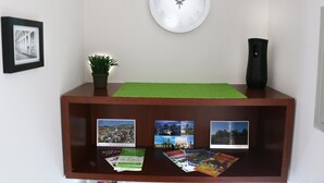 A wooden reception desk with a clock, framed picture, potted plant, and travel brochures. - Chile4Rent Eleuterio Ramirez (Santiago)