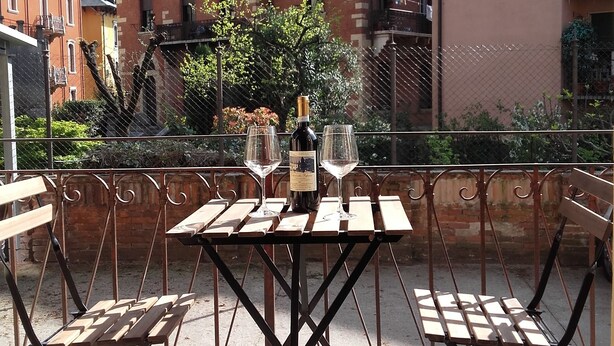 A patio with a table set for two, featuring a bottle and glasses, surrounded by metal railings and benches. - Verona4rent Roberto (Verona)