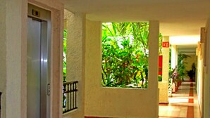 A corridor with a tiled floor, a door on the left, a window with greenery, and a red sign on the wall. - 2 BR w Balcony Apartment Rinconada Del Sol (Playa del Carmen)