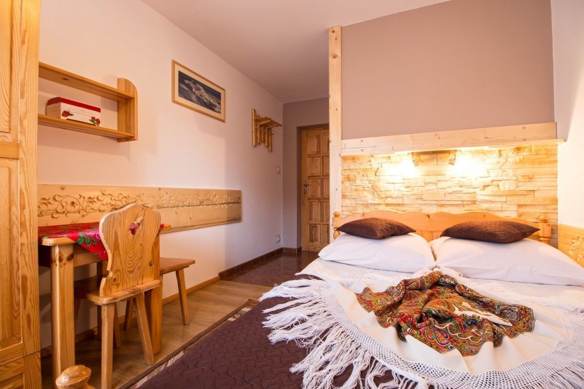 A bedroom with a wooden headboard, a bed with white linens, a colorful throw blanket, and a wooden chair.