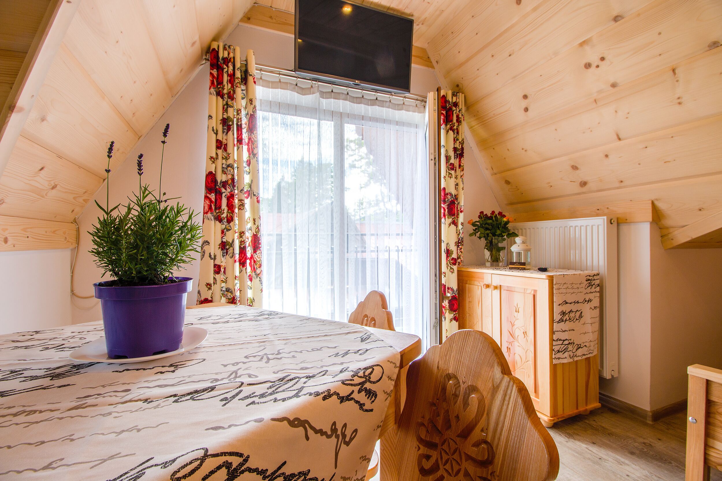 A cozy room with a sloped ceiling, a wooden table with a potted plant, a cabinet, and a radiator.