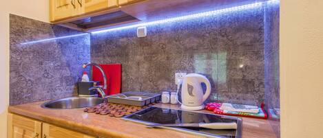 A kitchen with wooden cabinets, a stainless steel sink, a kettle, and a tablet on the counter.