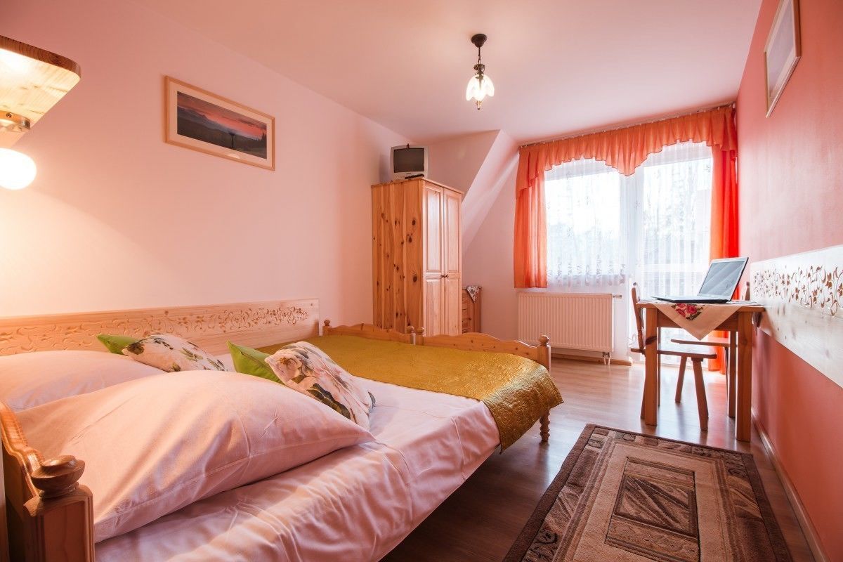 Een slaapkamer met twee bedden, een houten garderobe, een bureau met een laptop en een raam met gordijnen.
