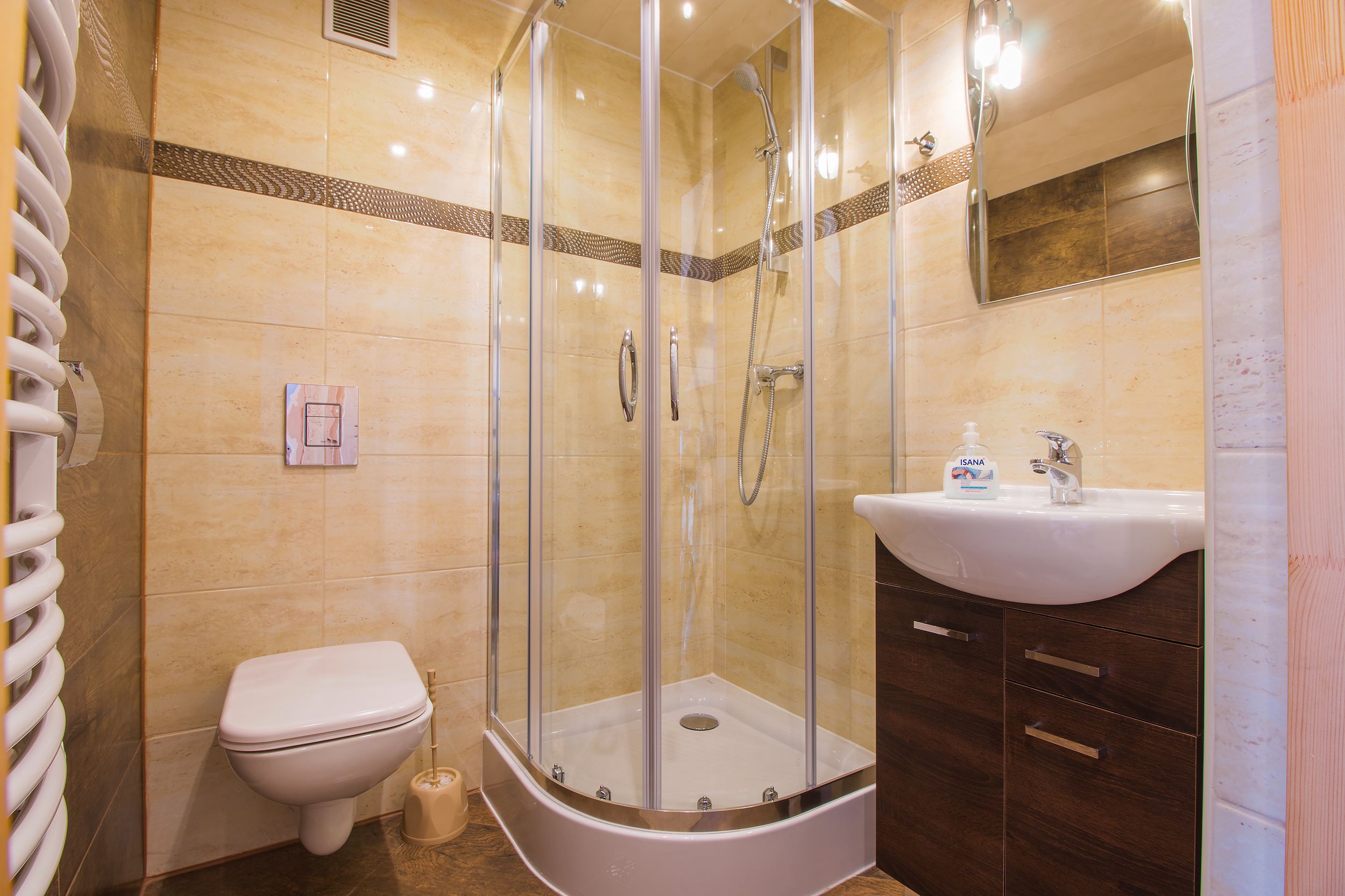 A bathroom with a glass-enclosed shower, a white toilet, a sink with a soap dispenser, and a mirror above the sink.