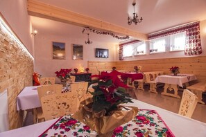 A cozy dining area with wooden tables and chairs, a large plant centerpiece, and a rustic stone wall. - Willa Trebunia (Zakopane)