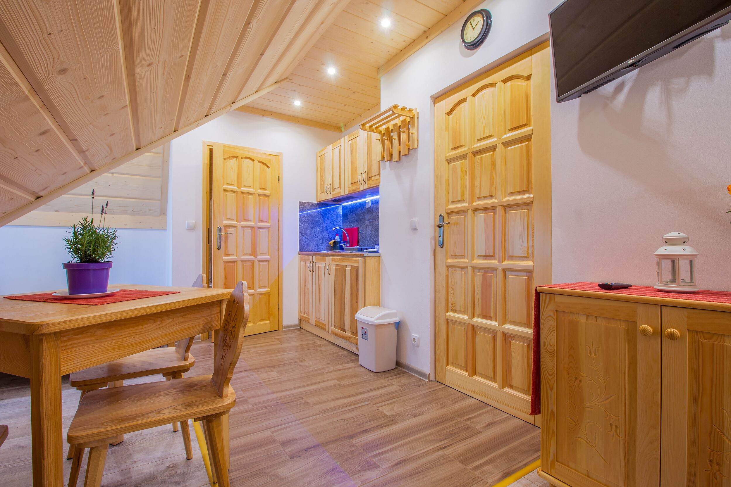 A wooden kitchen with a dining area, wooden cabinets, and a small trash bin.