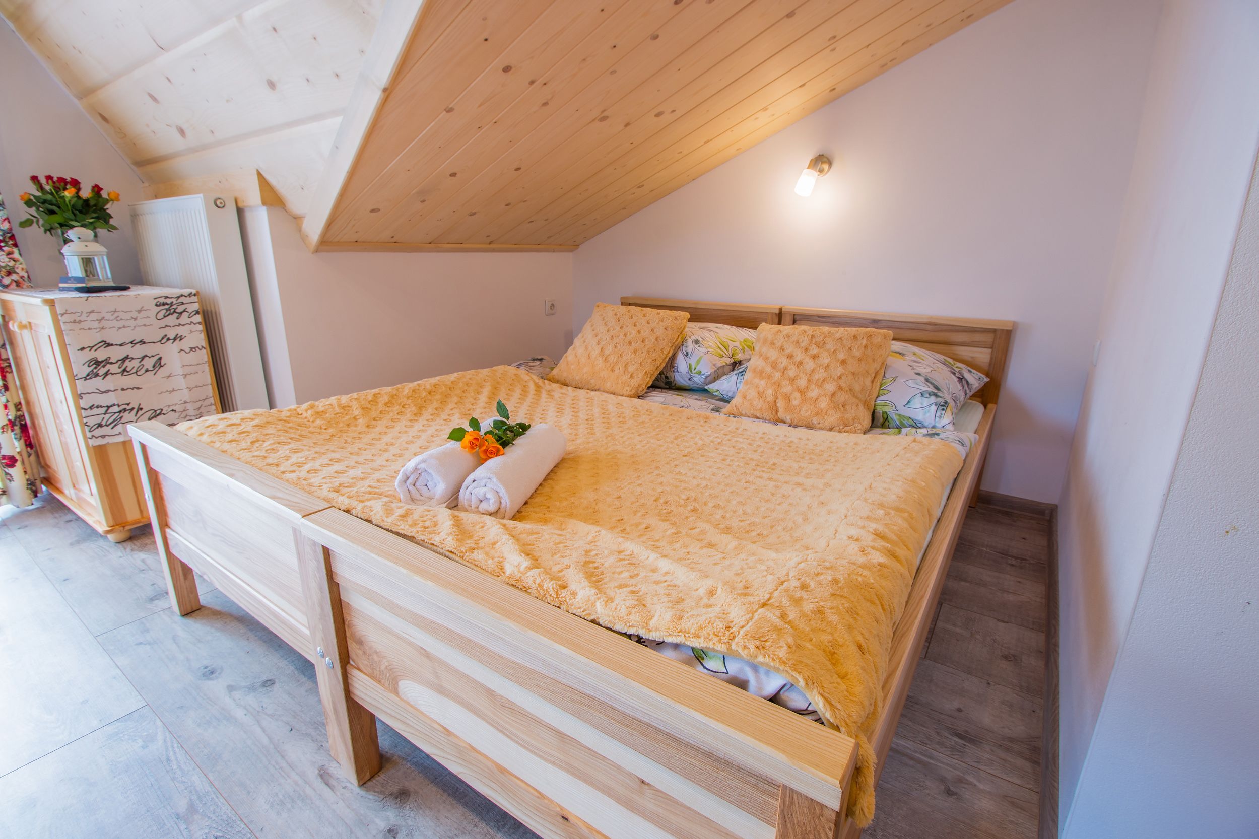 Una cama de madera con cabecera, una mesita de noche con lámpara y una pequeña planta en el buró.