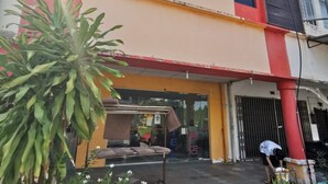 A two-story building with a red and yellow facade, a gated entrance, and a person working near the entrance. - OYO 90086 My Seven Days Inn (Masai)