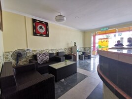 A lobby with wicker furniture, a fan, a framed artwork, and a reception desk.