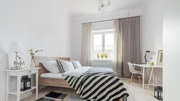 A modern bedroom with a bed, bedside table, lamp, and a view of the city through a window. - P&O Andersa (Warsaw)