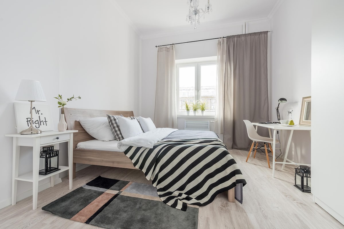 A modern bedroom with a bed, bedside table, lamp, and a view of the city through a window.