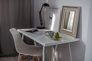 Uma mesa branca com um laptop, uma xícara e uma pera em um pires.
