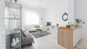 A modern living room with a glass cabinet, a grey sofa, a wooden dining table, and a white kitchen area. - P&O Andersa (Warsaw)