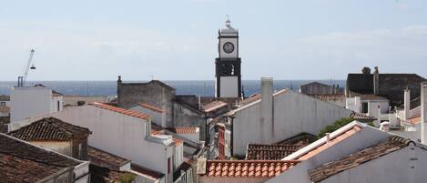 Vista de un paisaje urbano con una destacada torre del reloj, tejados de teja y un cielo despejado.