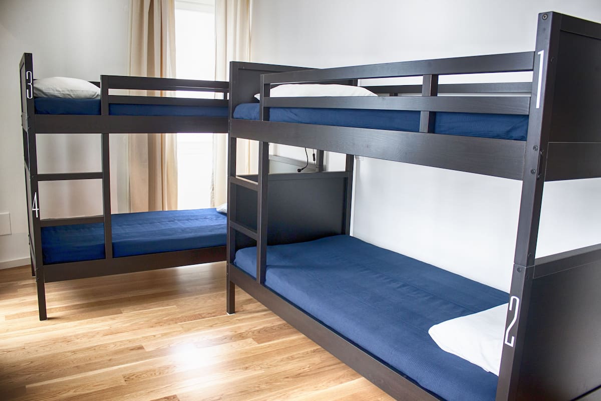 A room with two bunk beds, wooden flooring, and a window with curtains.